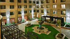 Un hotel de varios pisos con un patio central que incluye una fuente, asientos exteriores y un jardín iluminado.