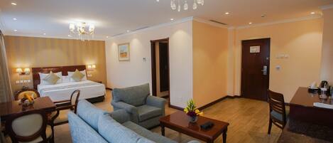 A hotel room with a bed, two sofas, a dining table, and a chandelier.