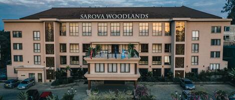 A multi-story hotel named Sarova Woodlands with a central entrance, balconies, and a parking area.