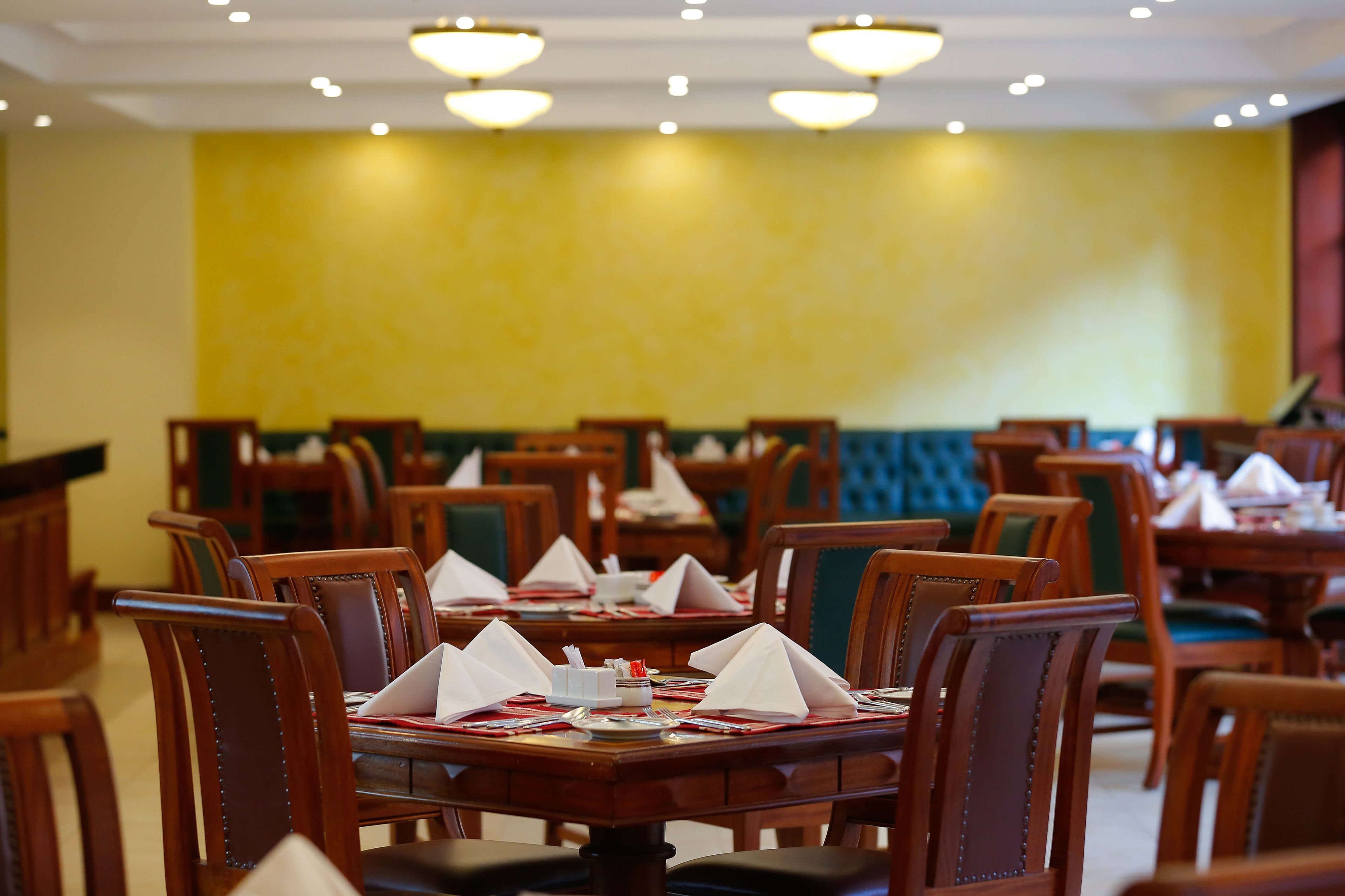 Un restaurant avec des tables et des chaises en bois, des murs jaunes et des banquettes vertes.