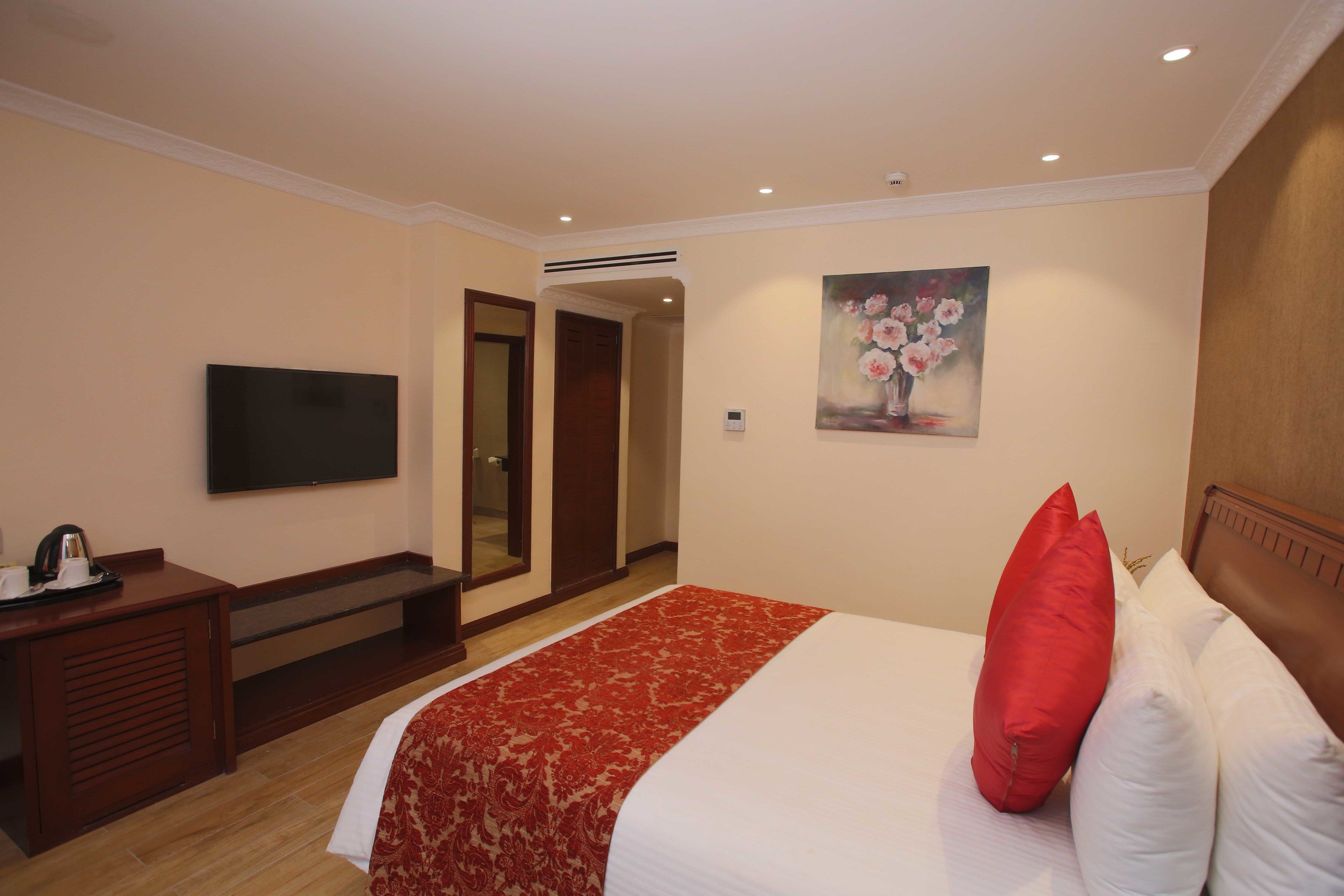 Een hotelkamer met een bed, een televisie, een bureau en een schilderij aan de muur.