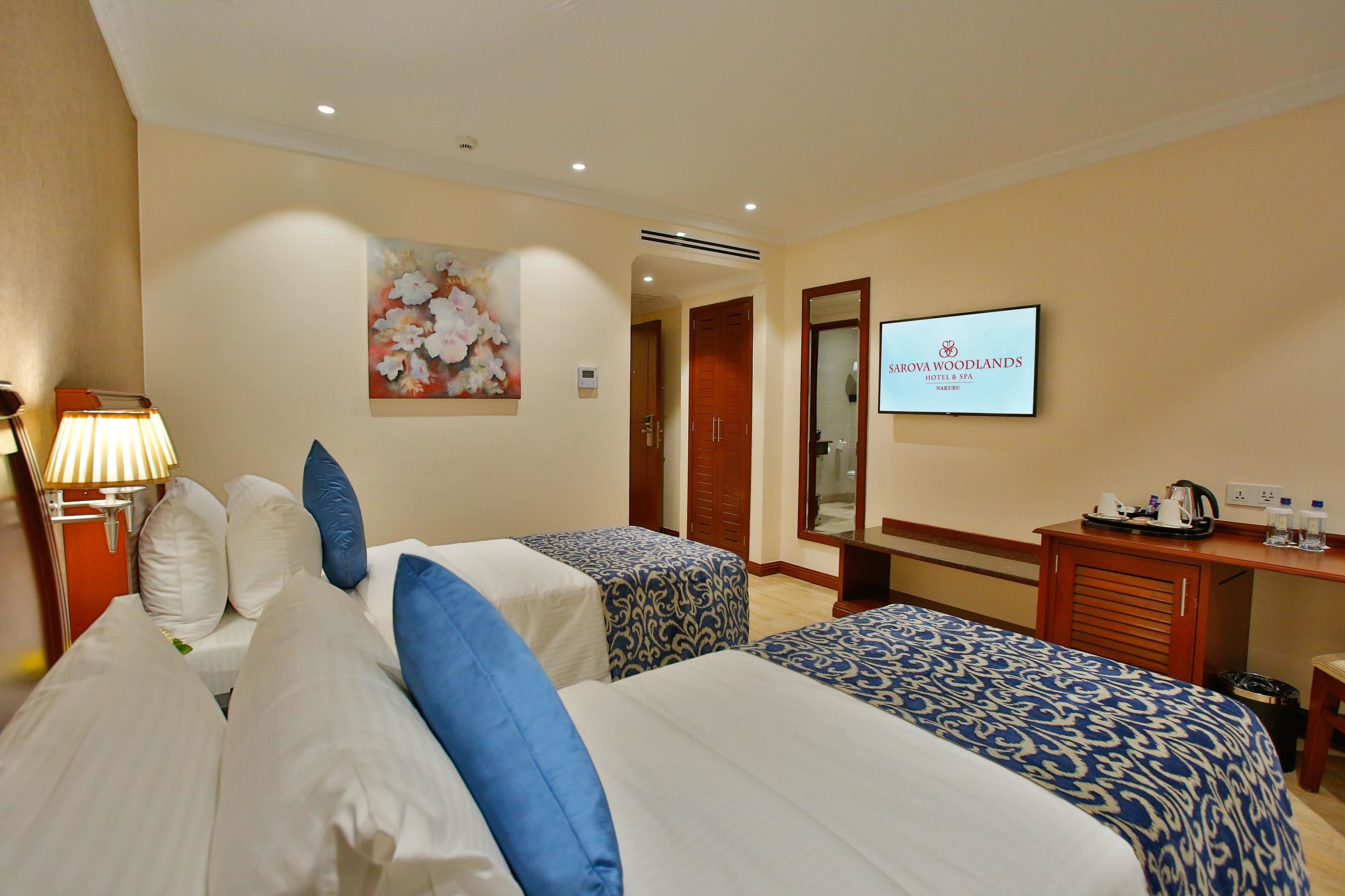 A hotel room with two beds, a desk with a television, and a painting on the wall.
