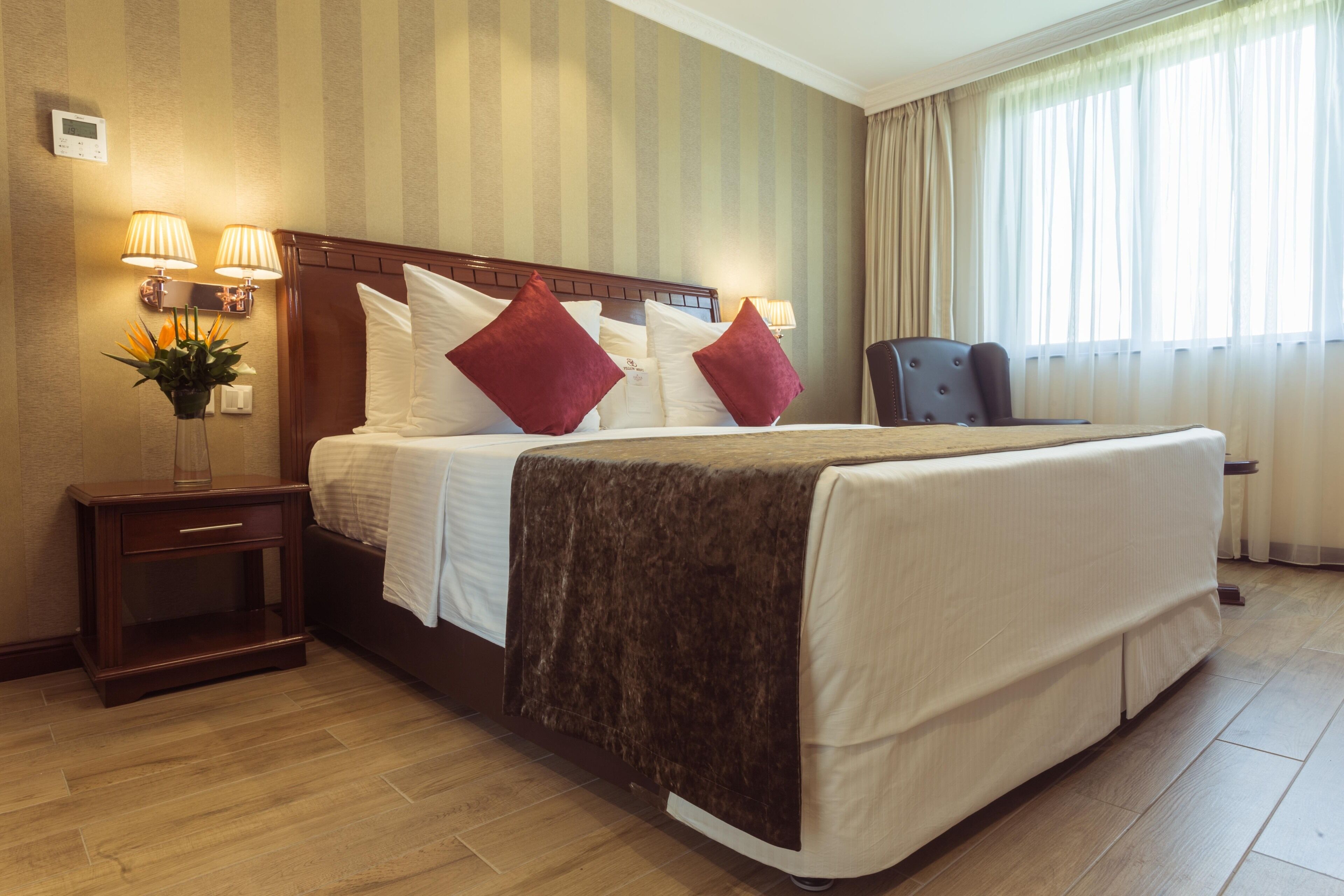 A hotel room with a large bed, two bedside lamps, a nightstand, a chair, and a window with curtains.