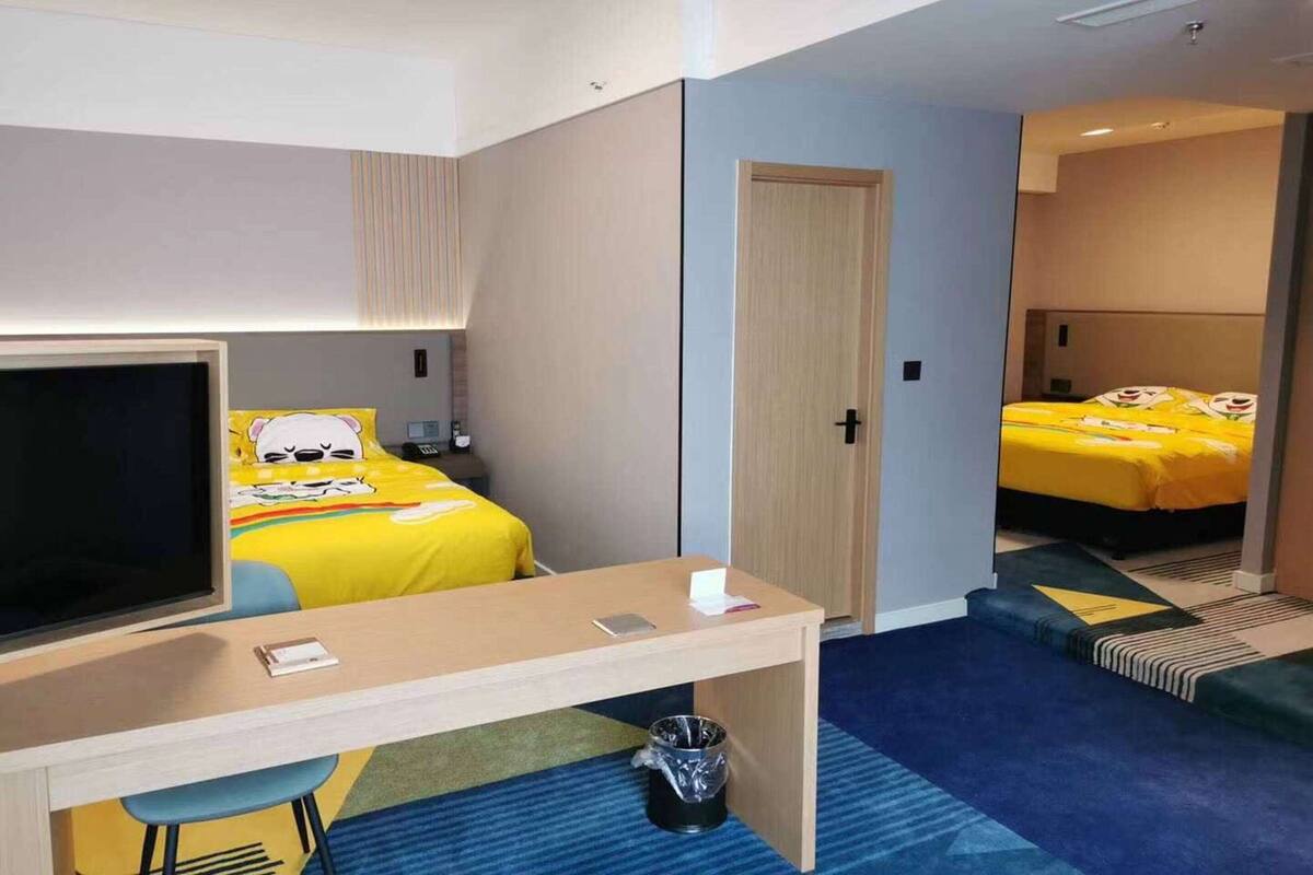 A hotel room with a bed, a desk, a TV, and a door.