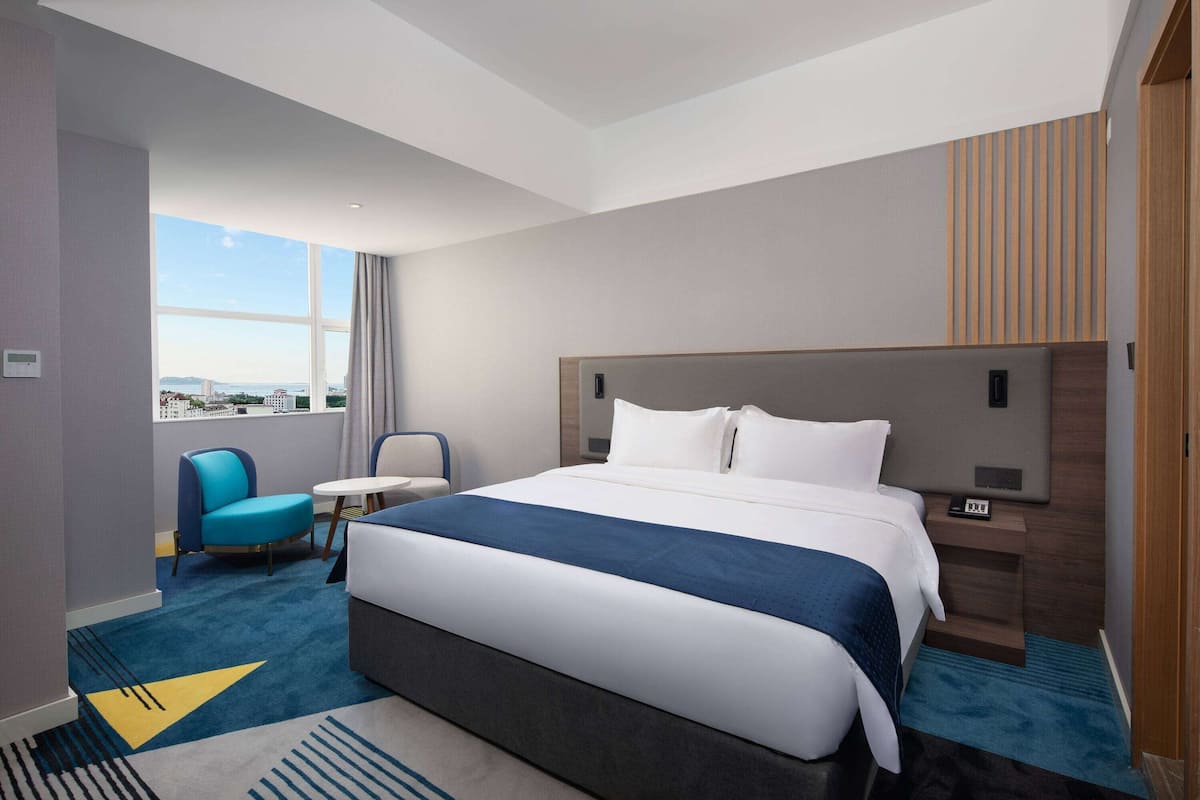 A hotel room with a large bed, a desk, a chair, and a view of the city.