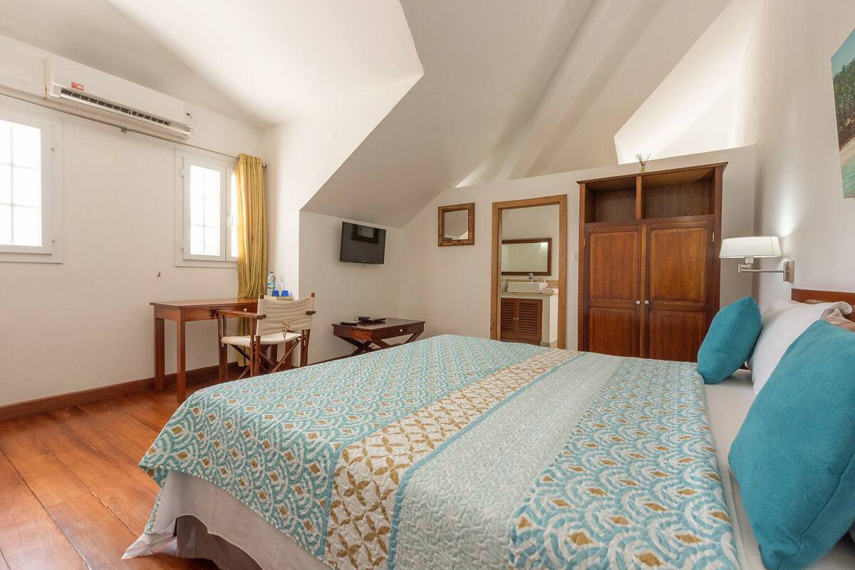 Ein Schlafzimmer mit einem Bett, einem Schreibtisch, einem Stuhl, einem Fernseher, einem Kleiderschrank und einem Badezimmer.