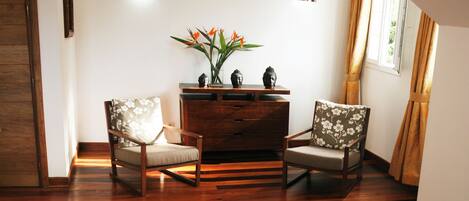 Una habitación con piso de madera, dos sillones tapizados, un armario de madera y un jarrón con flores.