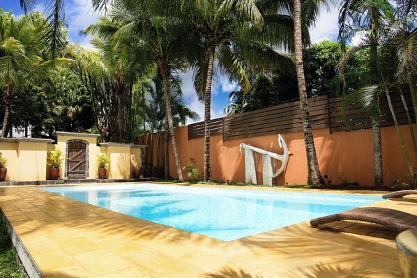 A swimming pool with a wooden fence, palm trees, and a brick wall. - Maison D'Hôtes Coignet (Beau Bassin - Rose Hill)