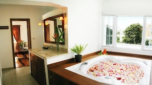 A bathroom with a large bathtub, a sink, a mirror, and a potted plant.