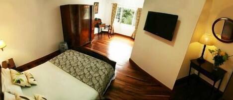Quarto com cama, escrivaninha, cadeira, televisão e janela.