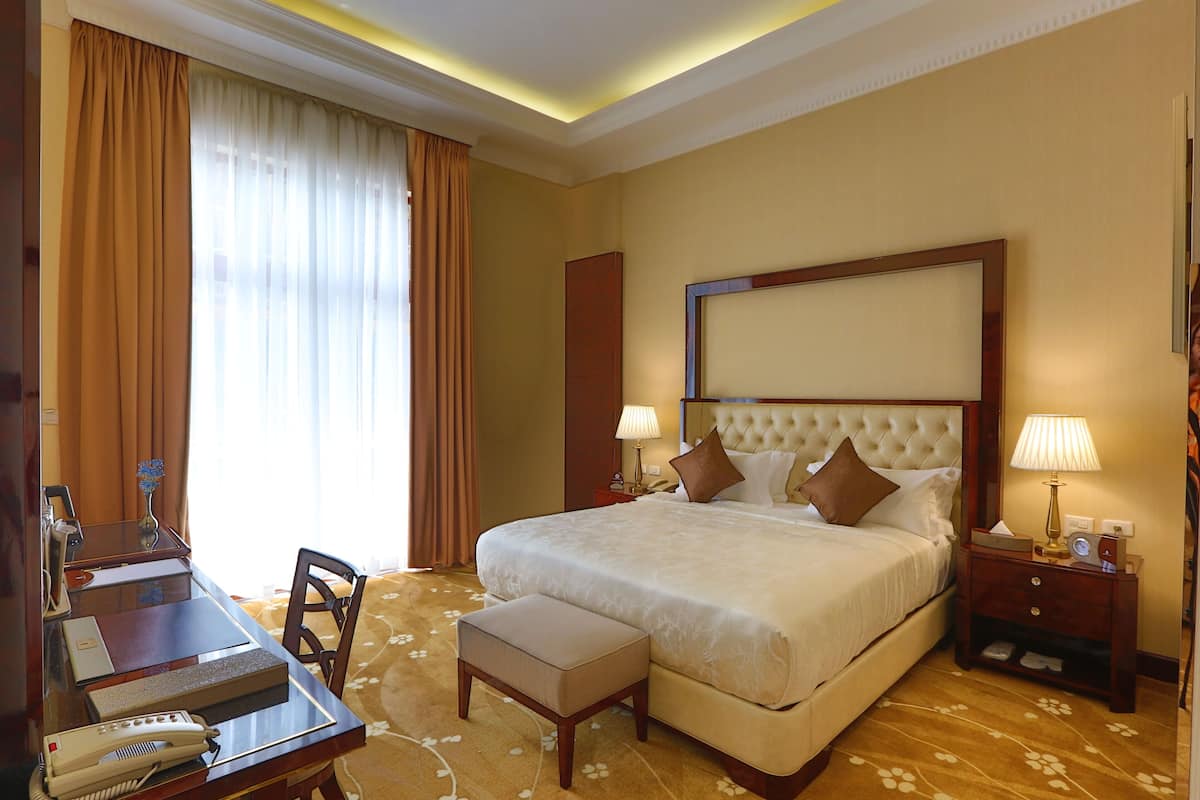 A hotel room with a large bed, bedside tables, a desk with a telephone, and a chair.