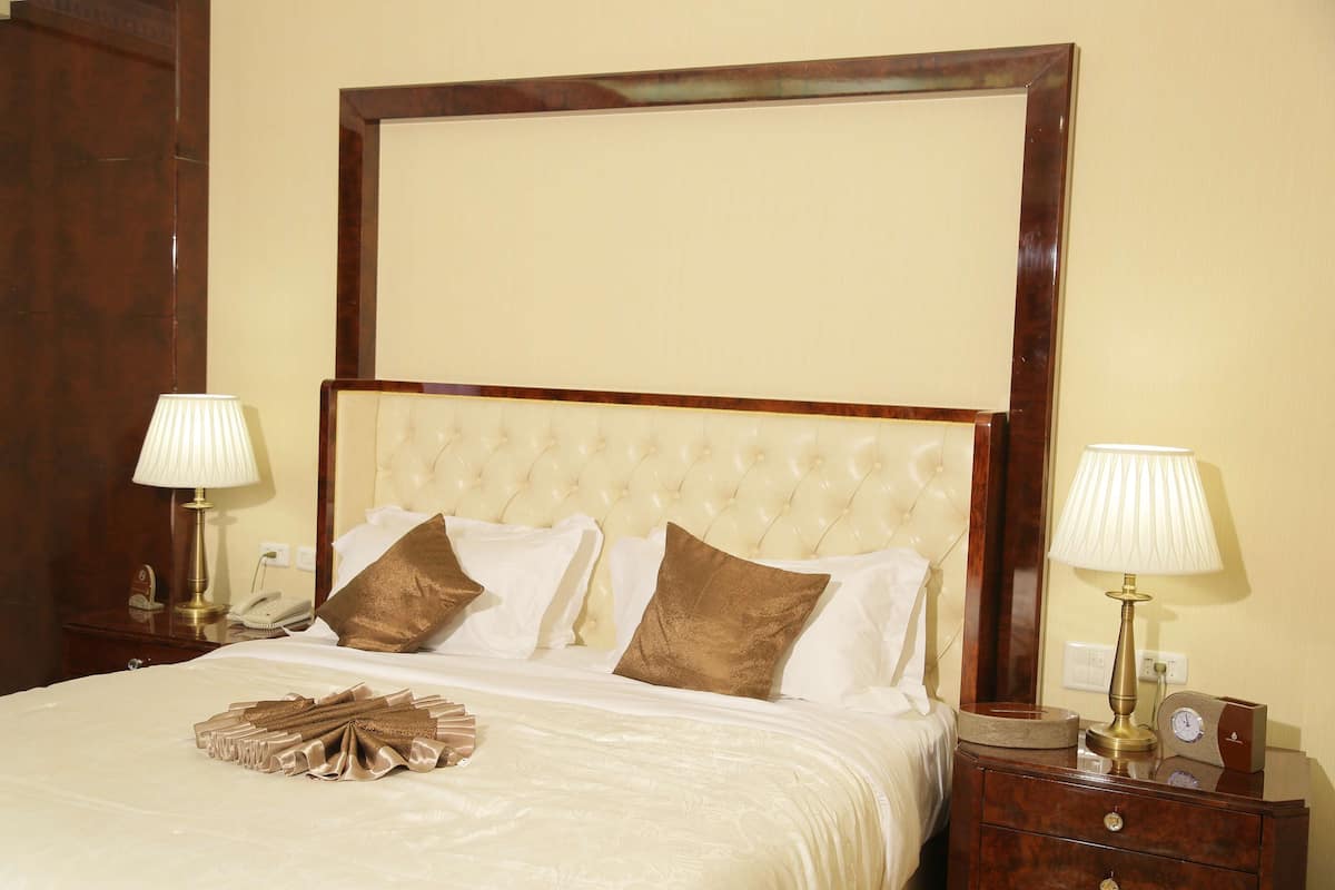 A neatly made bed with a tufted headboard, two bedside lamps, and a bedside table with a clock and a phone.