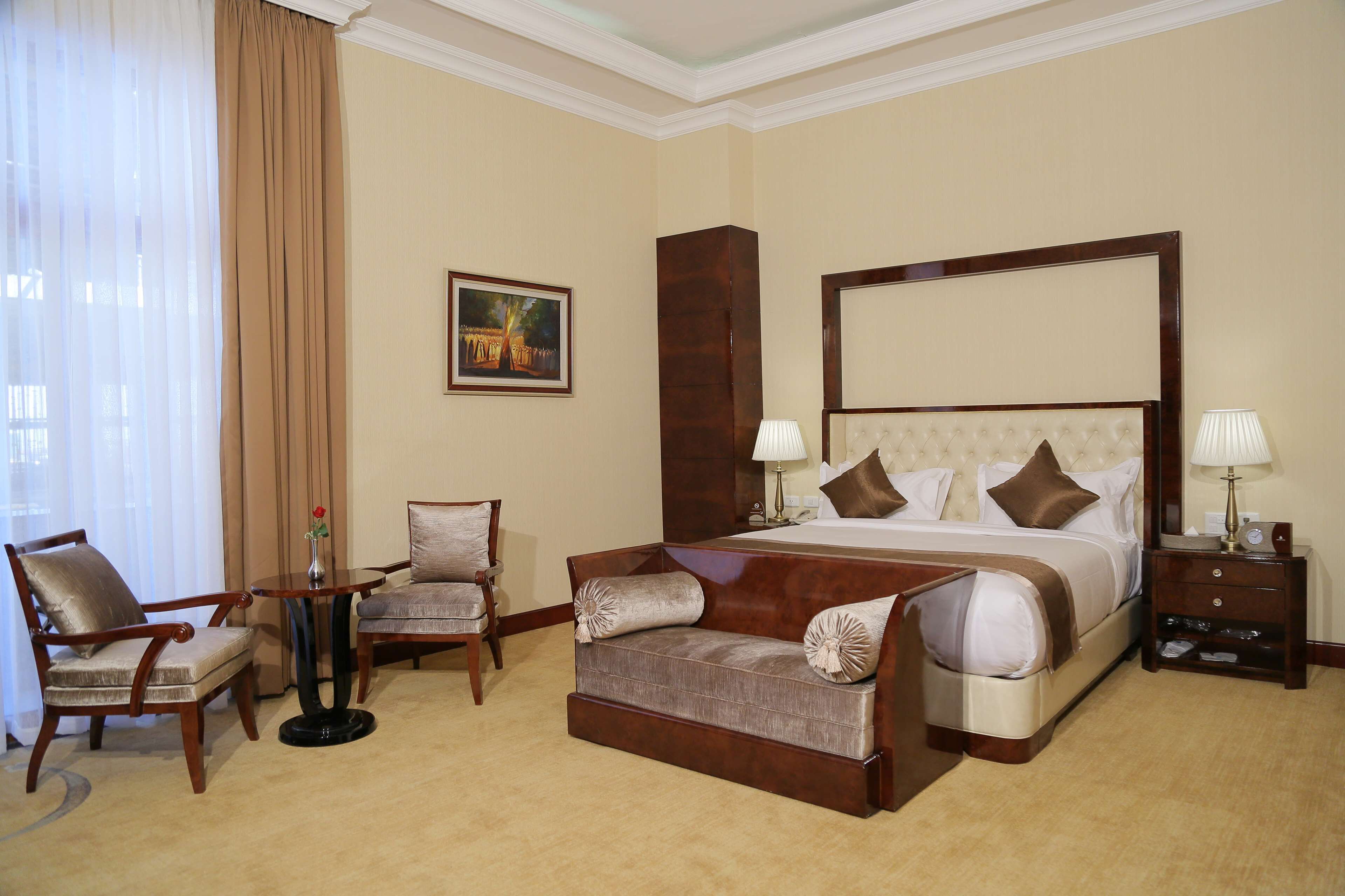 A hotel room with a large bed, two armchairs, a small table, and a nightstand.