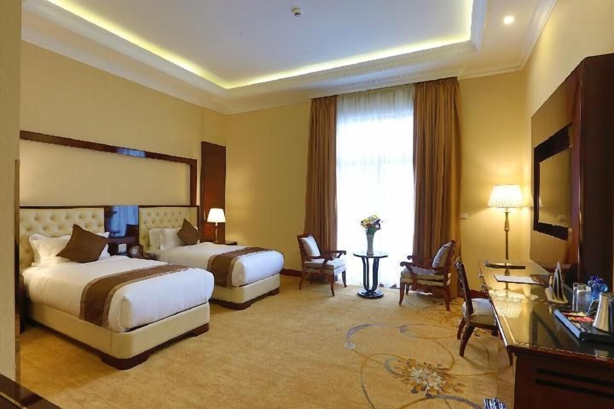 A hotel room with two beds, a sitting area with a table and chairs, a television, and a large mirror.