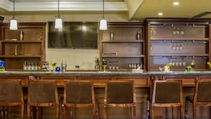 A bar area with wooden bar stools, a countertop with various bar tools, and shelves with glassware.