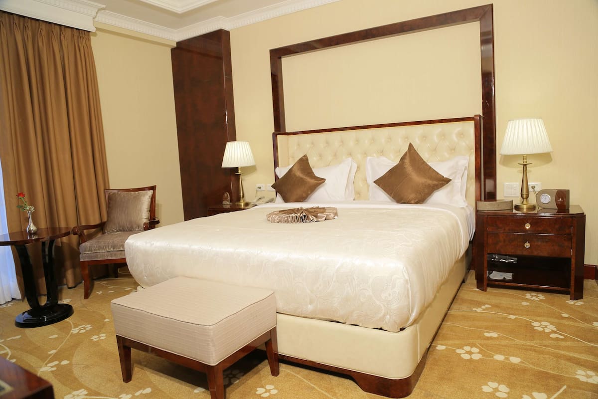 A hotel room with a large bed, two bedside tables, a chair, and a small table with a lamp.