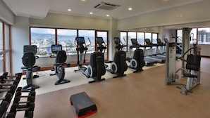 A gym with treadmills, elliptical machines, and weight stations, large windows with a city view.