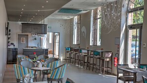 A modern restaurant interior with striped chairs, tables set for dining, and large windows allowing natural light. - Hôtel de la Tabletterie (Meru)