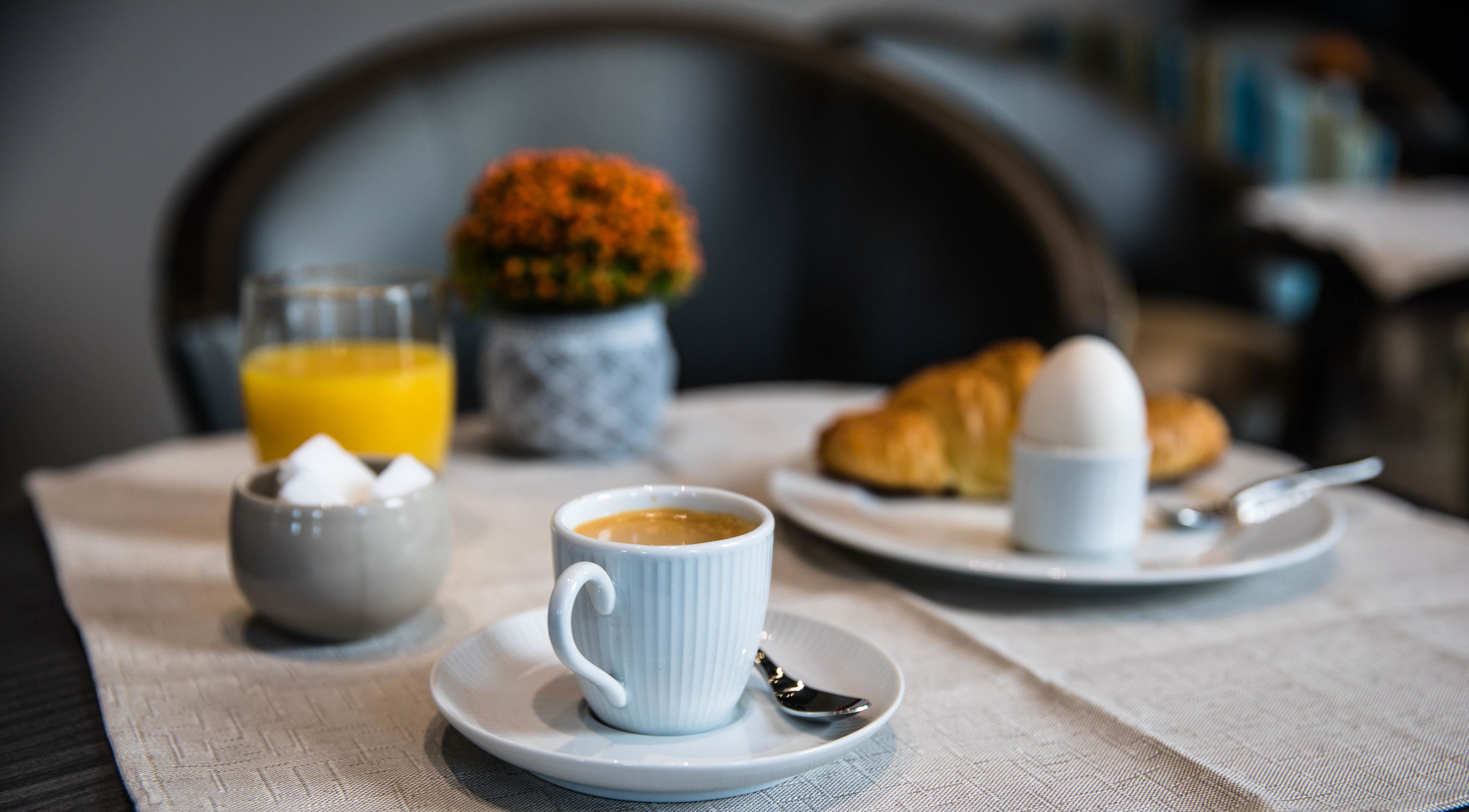 Un esmorzar amb una tassa de cafè, un croissant i un got de suc d'aranja sobre una taula.