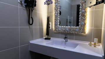 Un baño con lavamanos blanco, secador de pelo y espejo decorativo con conchas marinas.