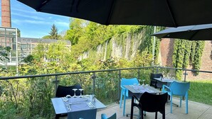 An outdoor dining area with tables and chairs, a view of greenery and buildings in the background. - Hôtel de la Tabletterie (Meru)