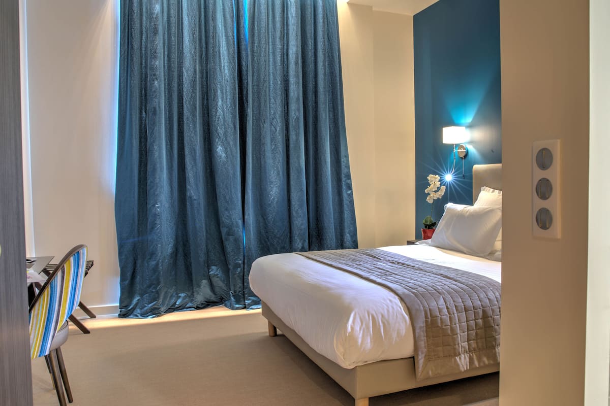 A bedroom with a bed, a nightstand, a lamp, and a window with curtains.