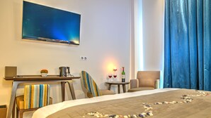 A hotel room with a bed, a desk with a computer, a chair, a TV mounted on the wall, and a small table with a bottle and glasses. - Hôtel de la Tabletterie (Meru)