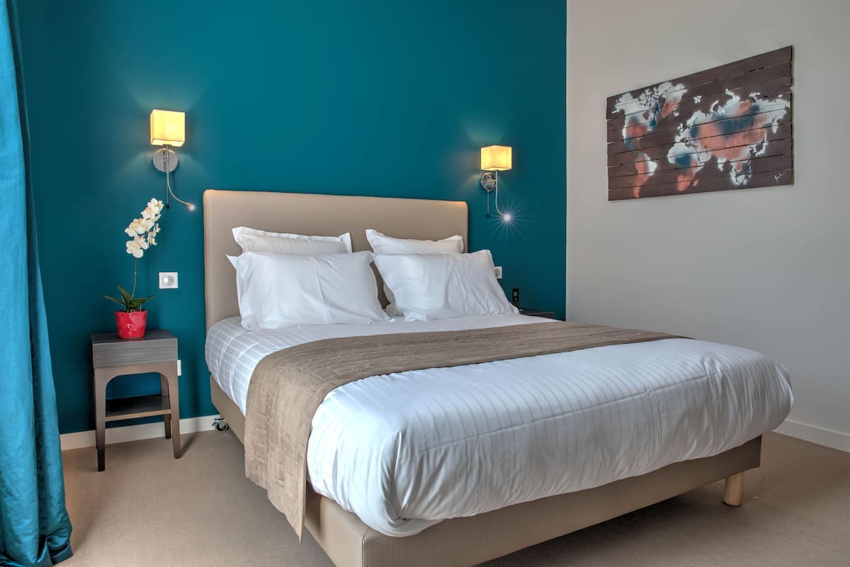 A bedroom with a bed, two wall-mounted lamps, a small stool with a plant, and a world map artwork on the wall.