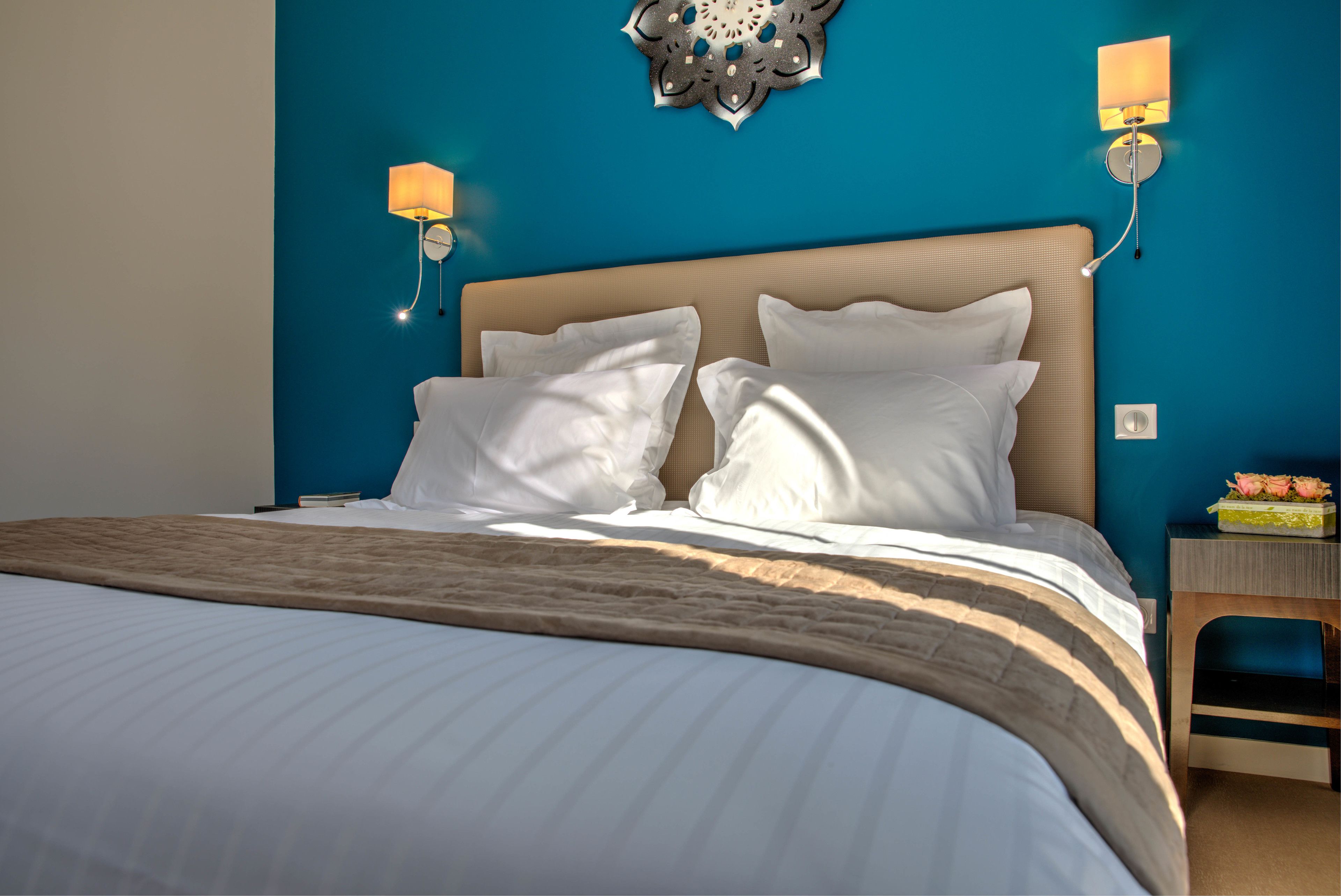 Una cama bien hecha con sábanas blancas, cabecera color beige y un elemento decorativo en la pared superior.