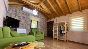 Una sala de estar acogedora con pared de ladrillo, vigas de madera en el techo, un sofá verde, una mesa de madera y un televisor montado en la pared.