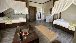 Una habitación con dos camas, una mesita con una botella y vasos, un armario y una puerta que da a un baño.