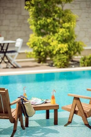 Zona de piscina con sillas y mesa de madera, una bebida y una pajita.