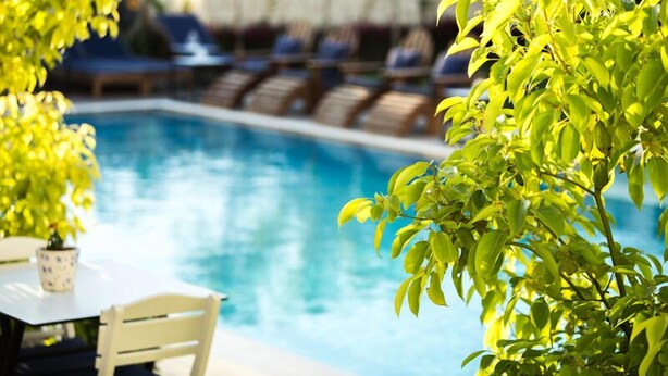 A poolside area with lounge chairs and a table, surrounded by greenery. - Levin Otel (Cesme)