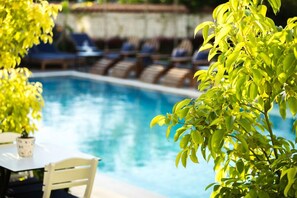 Un área junto a la piscina con sillones de descanso y una mesa, rodeada de follaje.