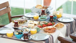 A breakfast table with various dishes, including bread, tomatoes, and a bowl of olives. - Levin Otel (Cesme)