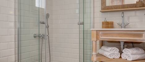A modern bathroom with a glass-enclosed shower, a white toilet, a wooden vanity with a mirror, and patterned floor tiles.