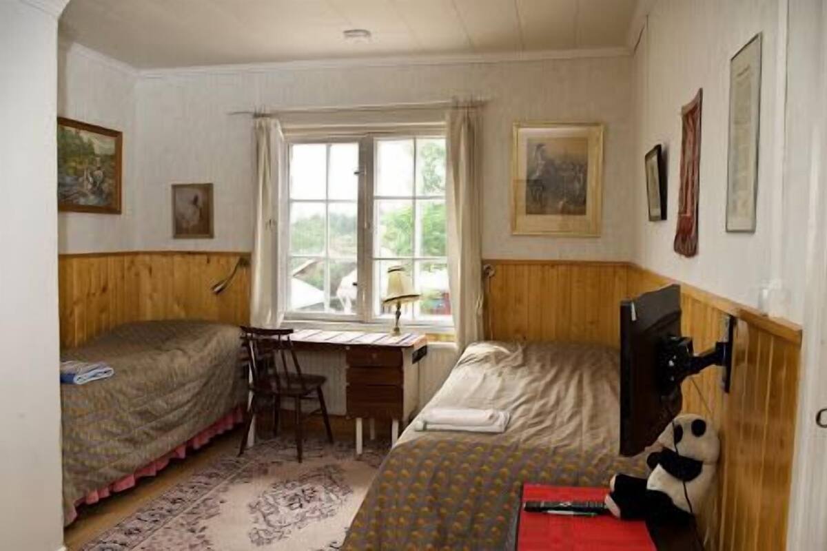 A room with two single beds, a desk, a chair, a TV, and a window.