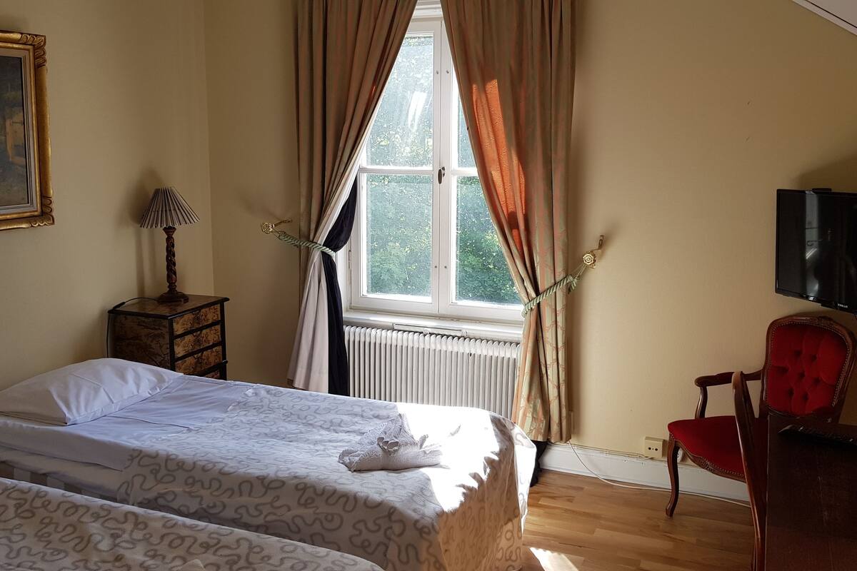 Un dormitorio con cama, una silla, un televisor y una ventana con cortinas.