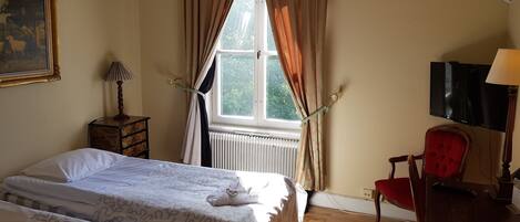 Un dormitorio con cama, una silla, un televisor y una ventana con cortinas.