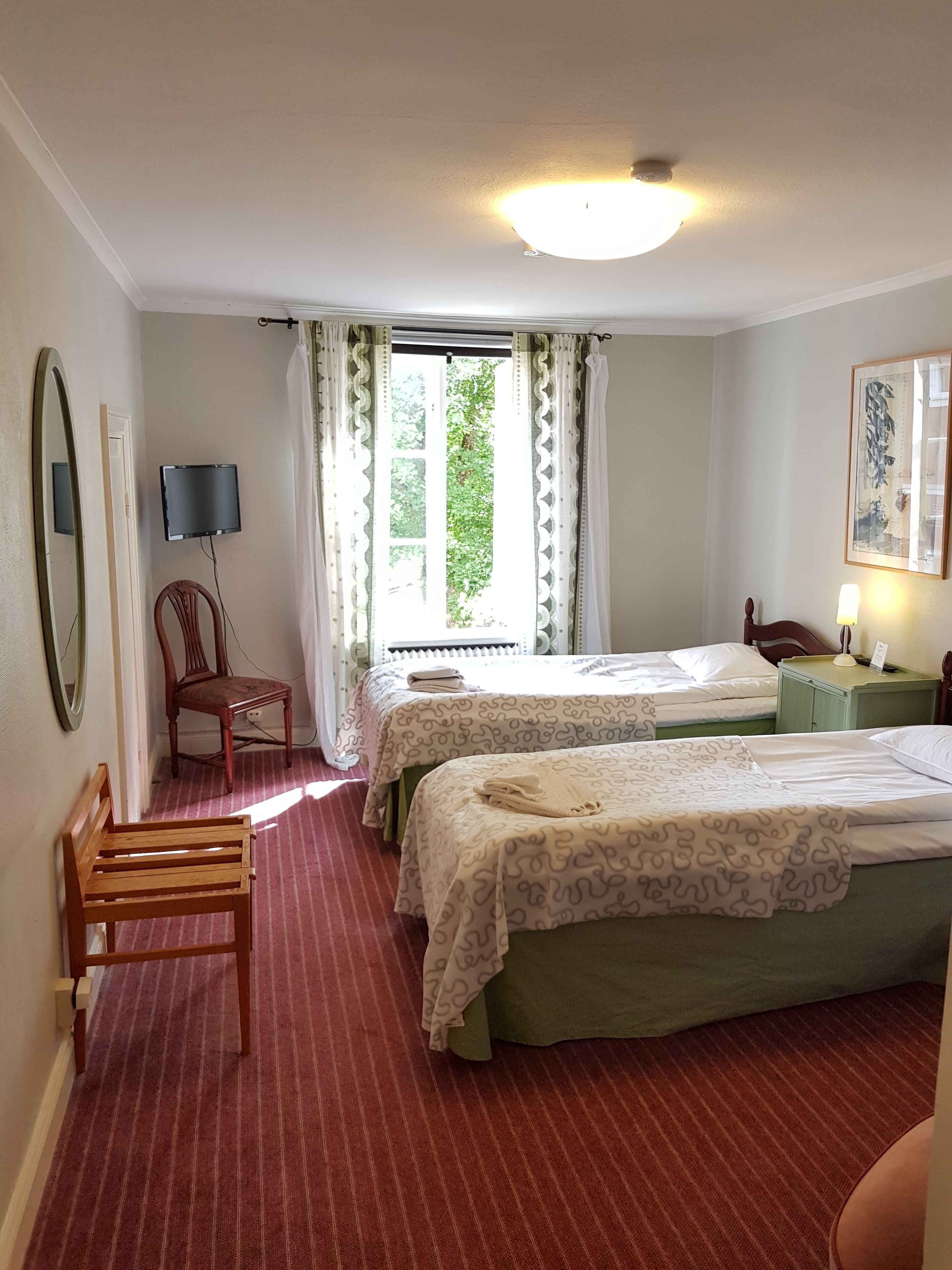 Een hotelkamer met twee bedden, een stoel, een bureau, een flatscreen televisie en een raam met gordijnen.