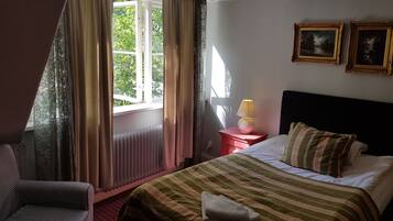 A hotel room with a bed, a chair, a nightstand with a lamp, and two framed pictures on the wall.