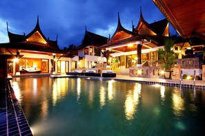 A traditional building with multiple roofs and a swimming pool in front.