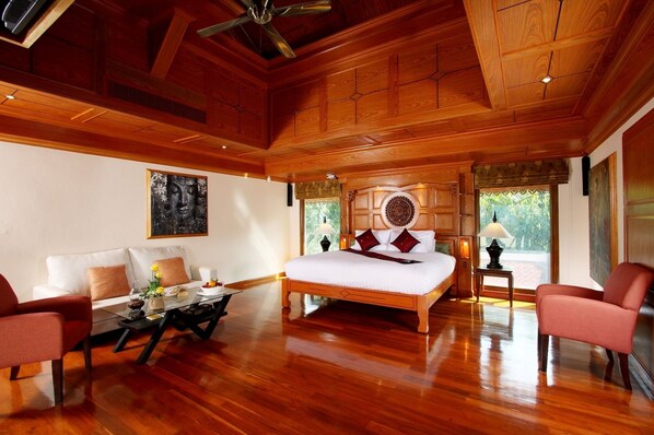 A spacious bedroom with a large bed, wooden ceiling, and a view of greenery outside.