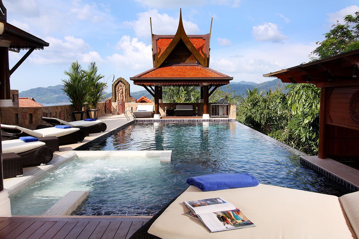 A pool area with lounge chairs and a covered seating area, surrounded by lush greenery and mountains in the background.
