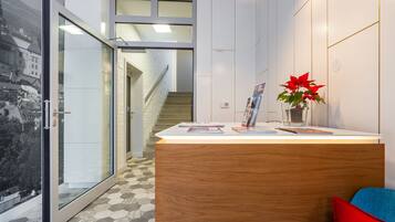 Un área de recepción con un mostrador de madera, una puerta de cristal que da a una escalera y una planta en maceta roja.
