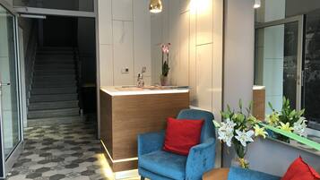 A reception area with a wooden desk, blue chairs, and a potted plant.