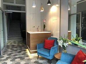 Un área de recepción con un escritorio de madera, sillas azules y una planta en maceta.