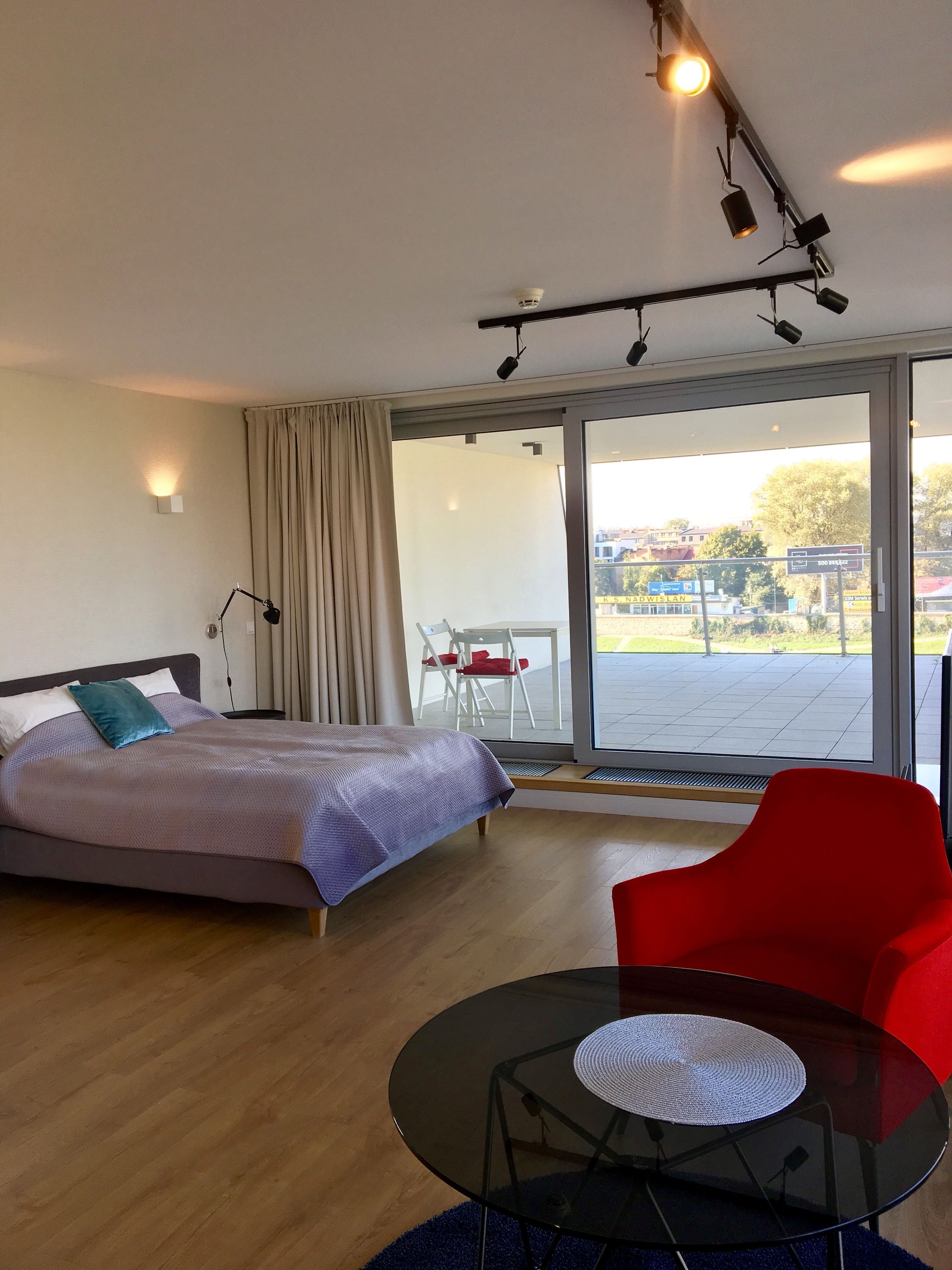 Une chambre d’hôtel moderne avec un lit, une chaise rouge, une table en verre et une vue sur l’extérieur.