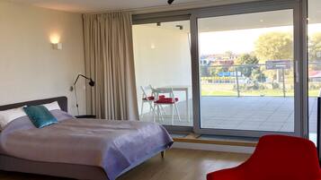 Une chambre d’hôtel moderne avec un lit, une chaise rouge, une table en verre et une vue sur l’extérieur.