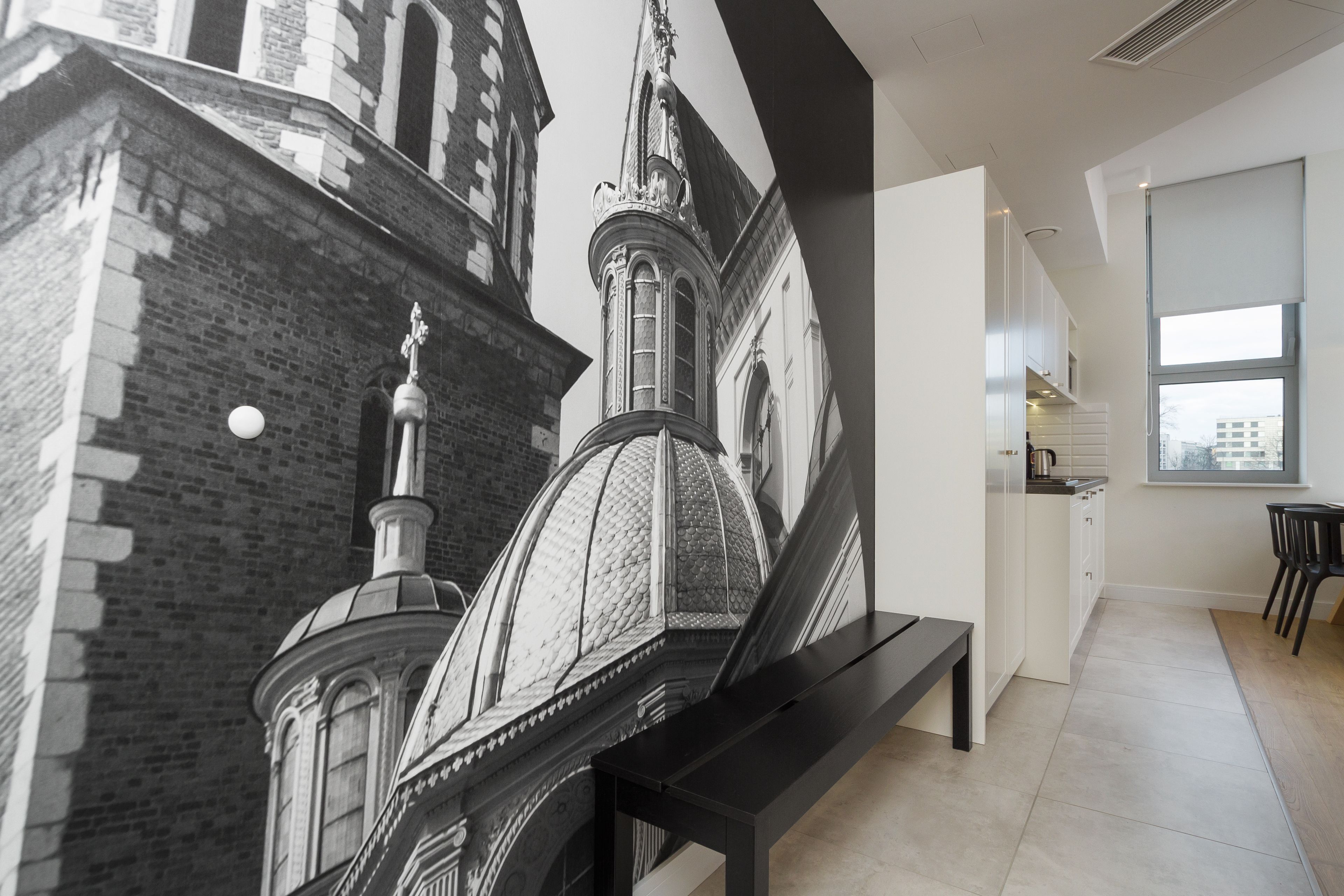 A modern interior with a large mural of a historical building, a kitchen area, and a dining space with a bench.